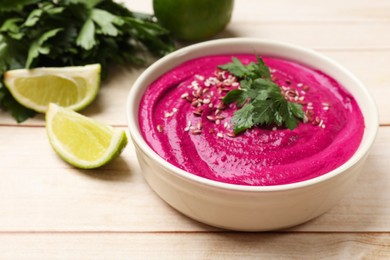 Photo of Tasty beetroot hummus, parsley and lime in bowl on light wooden table, closeup