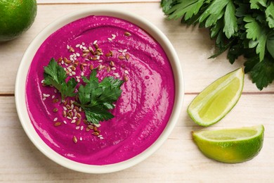 Photo of Tasty beetroot hummus, parsley and lime in bowl on light wooden table, flat lay