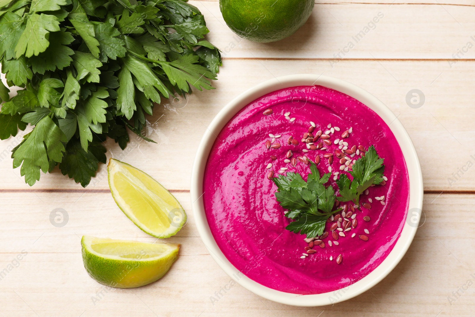 Photo of Tasty beetroot hummus, parsley and lime in bowl on light wooden table, flat lay