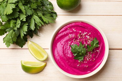 Photo of Tasty beetroot hummus, parsley and lime in bowl on light wooden table, flat lay