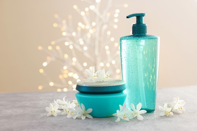 Photo of Cosmetic products and beautiful jasmine flowers on grey table. Space for text