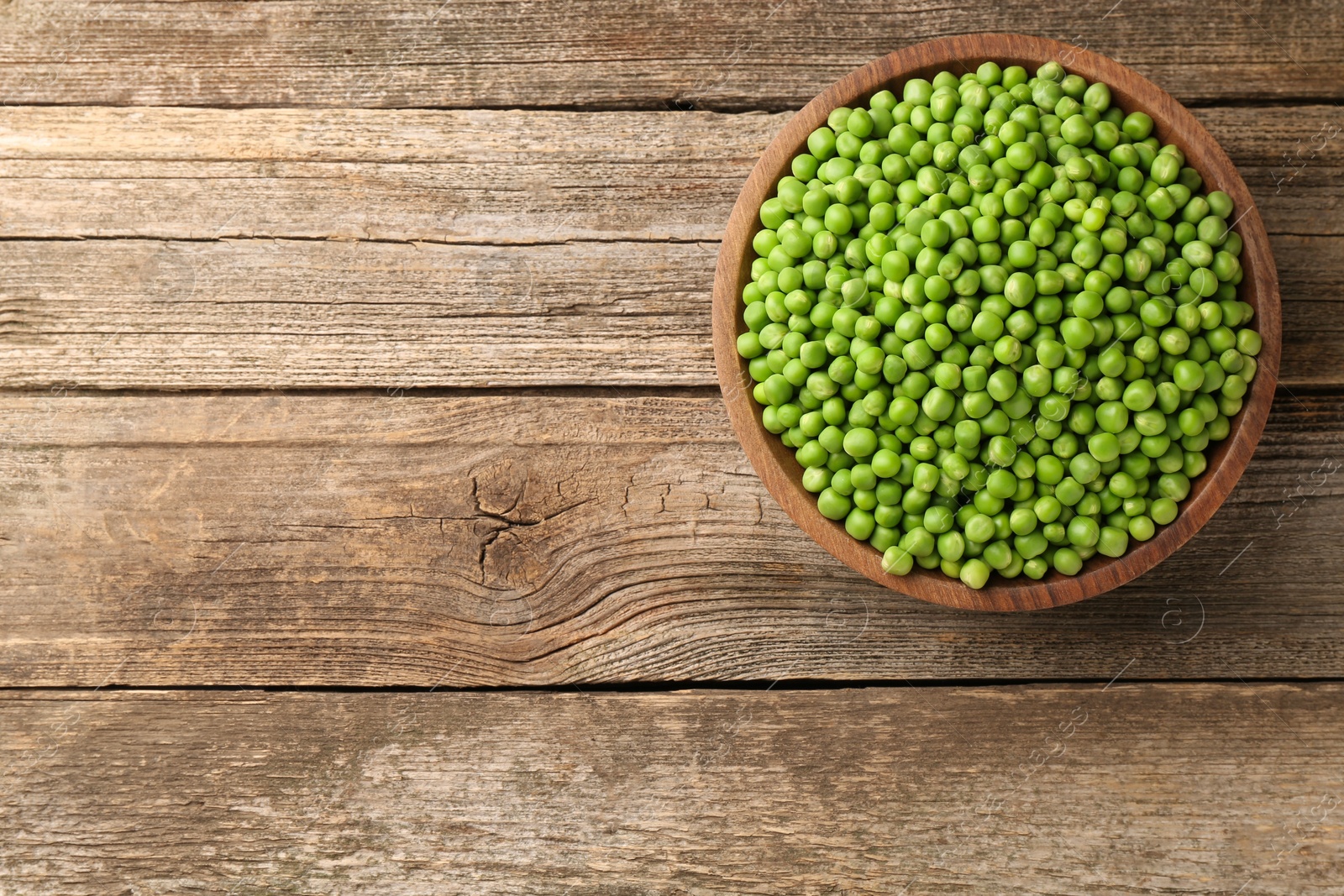 Photo of Fresh green peas in bowl on wooden table, top view. Space for text