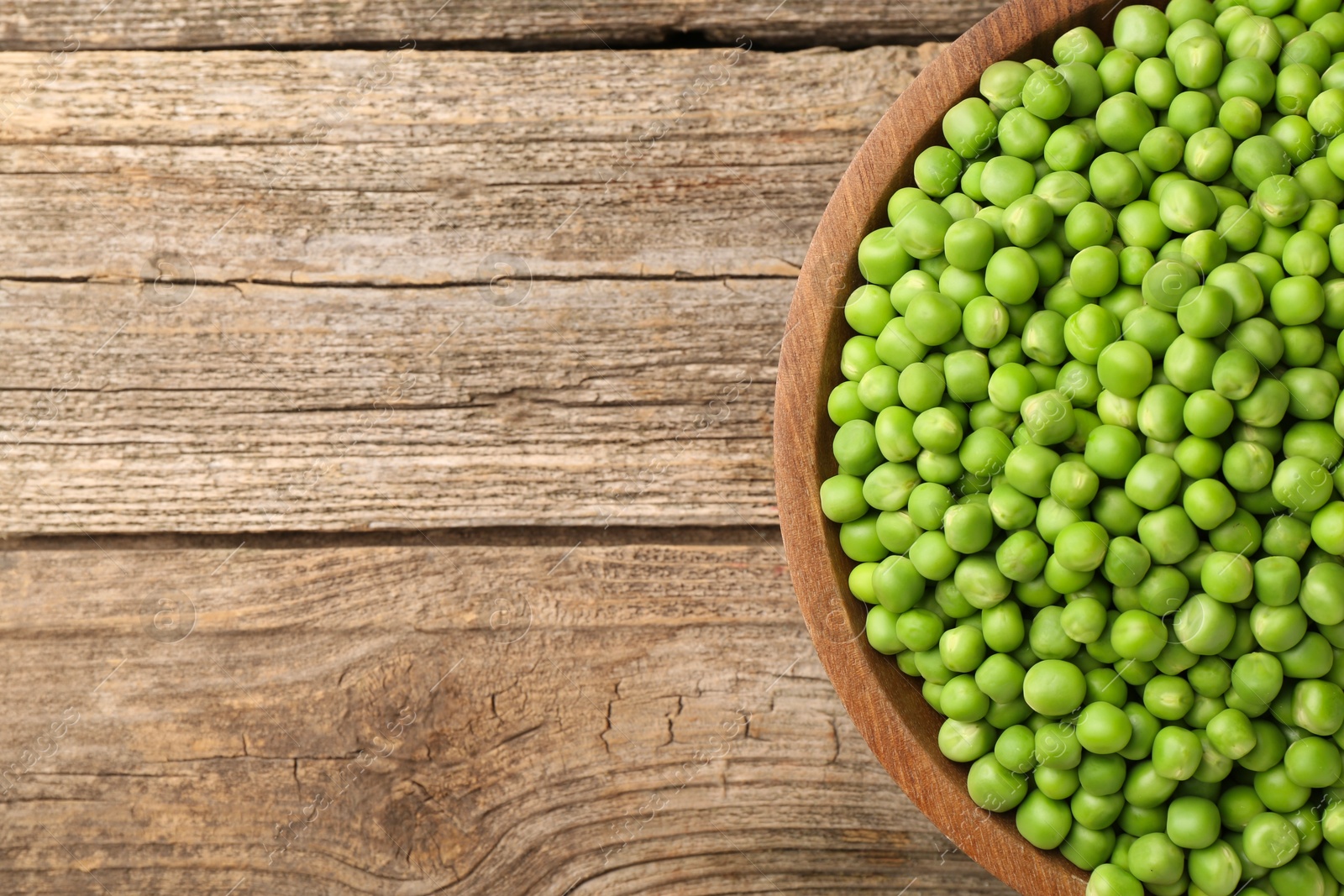 Photo of Fresh green peas in bowl on wooden table, top view. Space for text