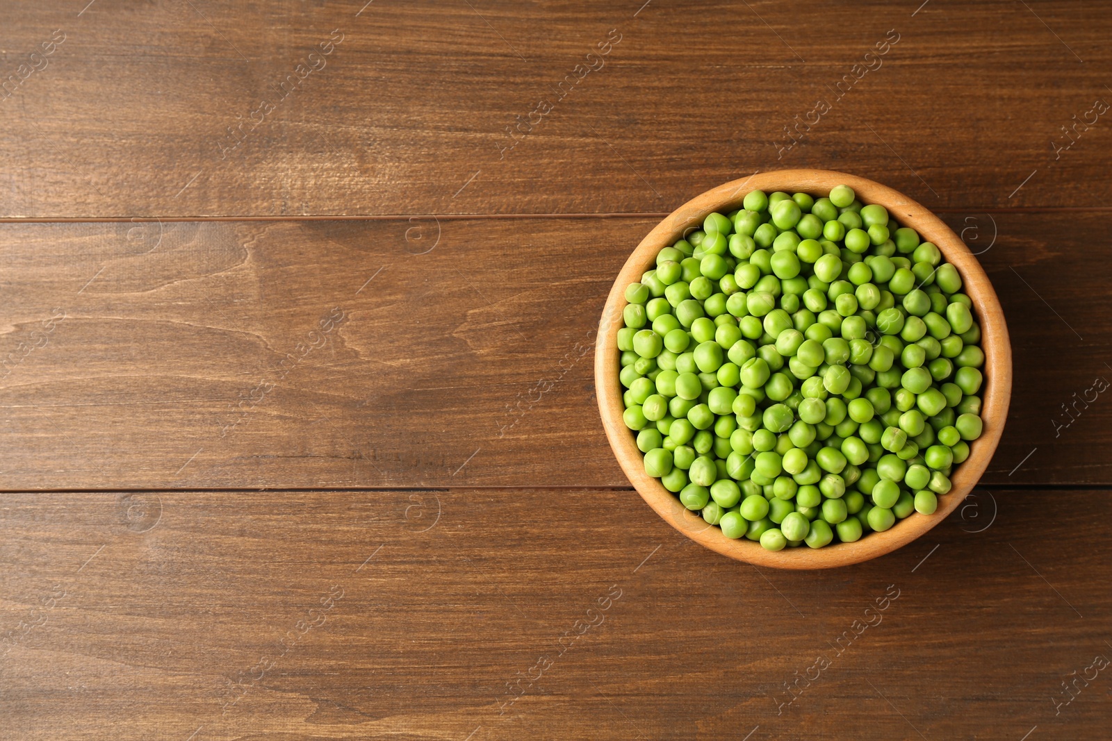 Photo of Fresh green peas in bowl on wooden table, top view. Space for text