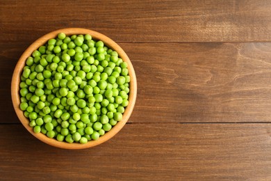 Photo of Fresh green peas in bowl on wooden table, top view. Space for text