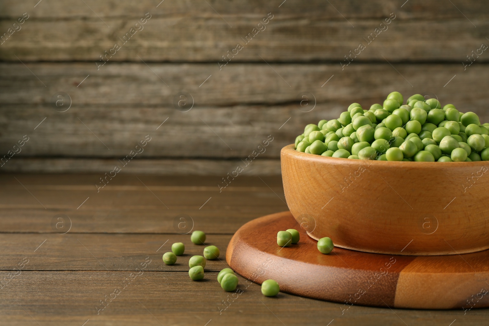 Photo of Fresh green peas in bowl on wooden table, space for text