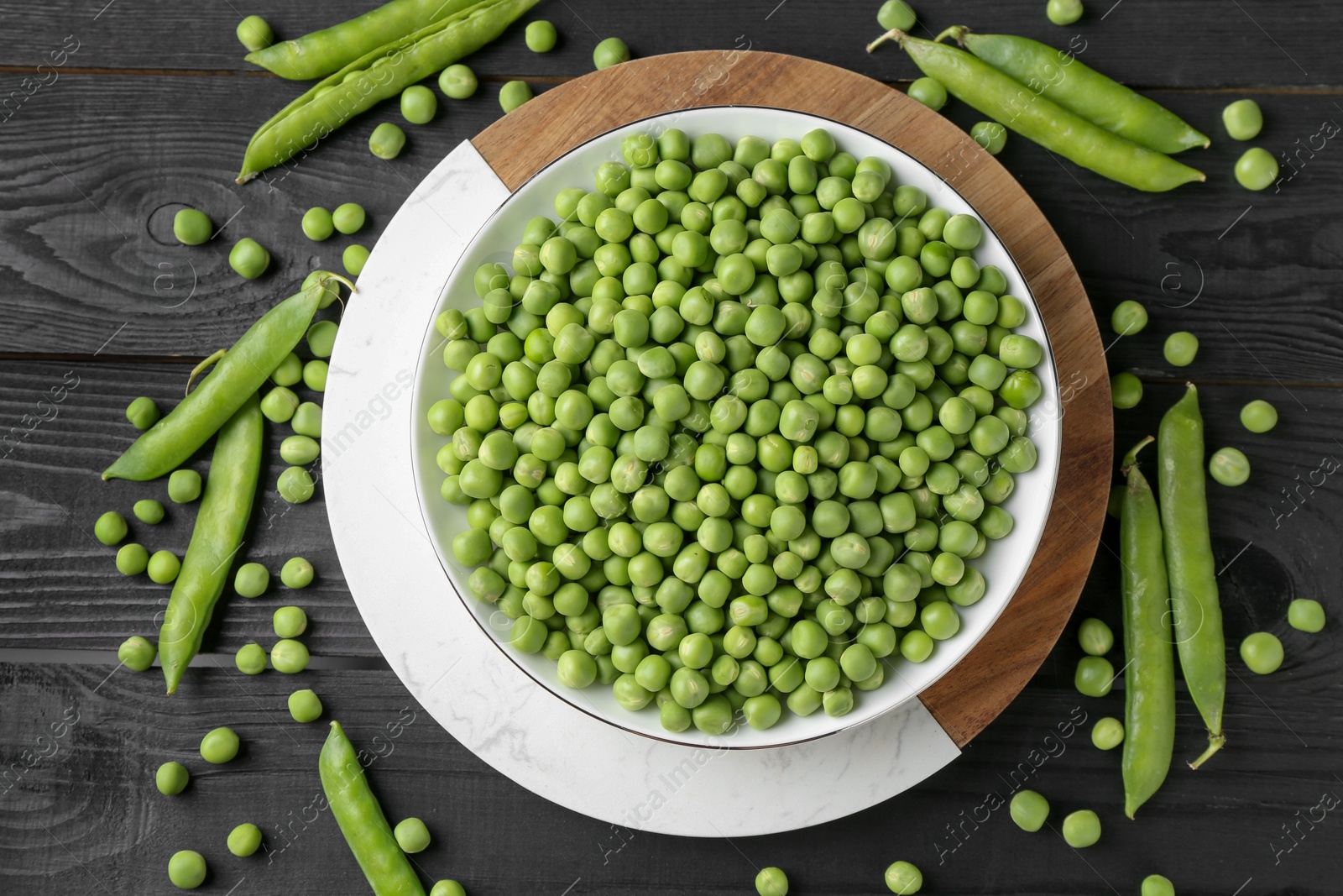 Photo of Fresh green peas in bowl and pods on black wooden table, flat lay