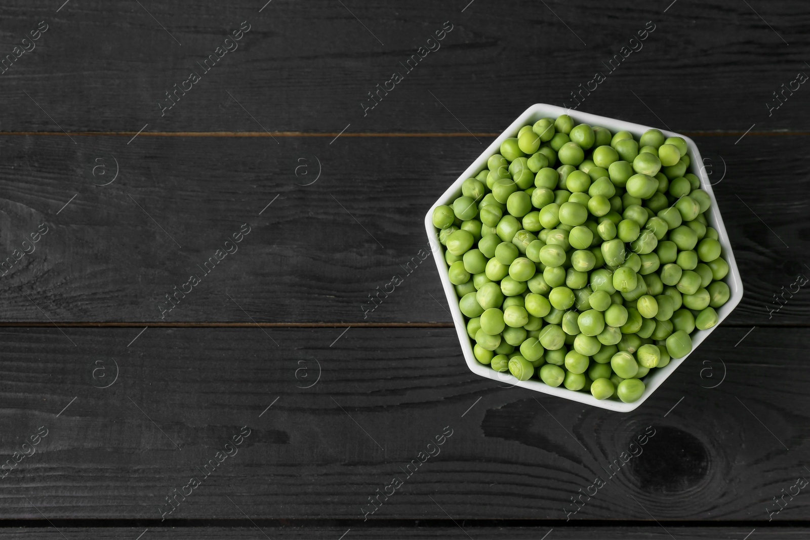 Photo of Fresh green peas in bowl on black wooden table, top view. Space for text