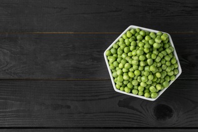 Photo of Fresh green peas in bowl on black wooden table, top view. Space for text