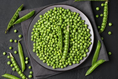 Photo of Fresh green peas and pods on black table, flat lay