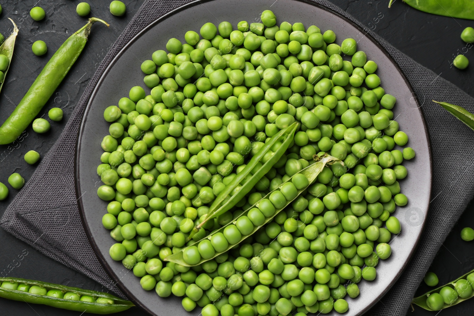 Photo of Fresh green peas and pods on black table, flat lay