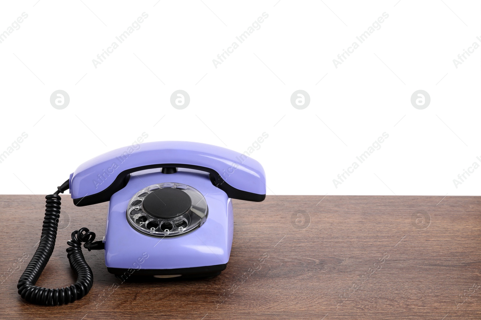 Photo of One violet telephone with handset on wooden table against white background