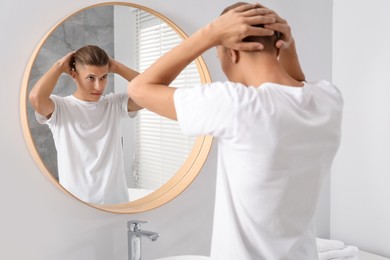 Handsome man looking at mirror in bathroom