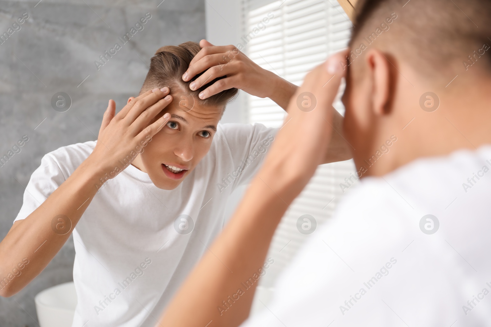 Photo of Man examining his hair and scalp near mirror in bathroom