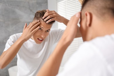 Man examining his hair and scalp near mirror in bathroom