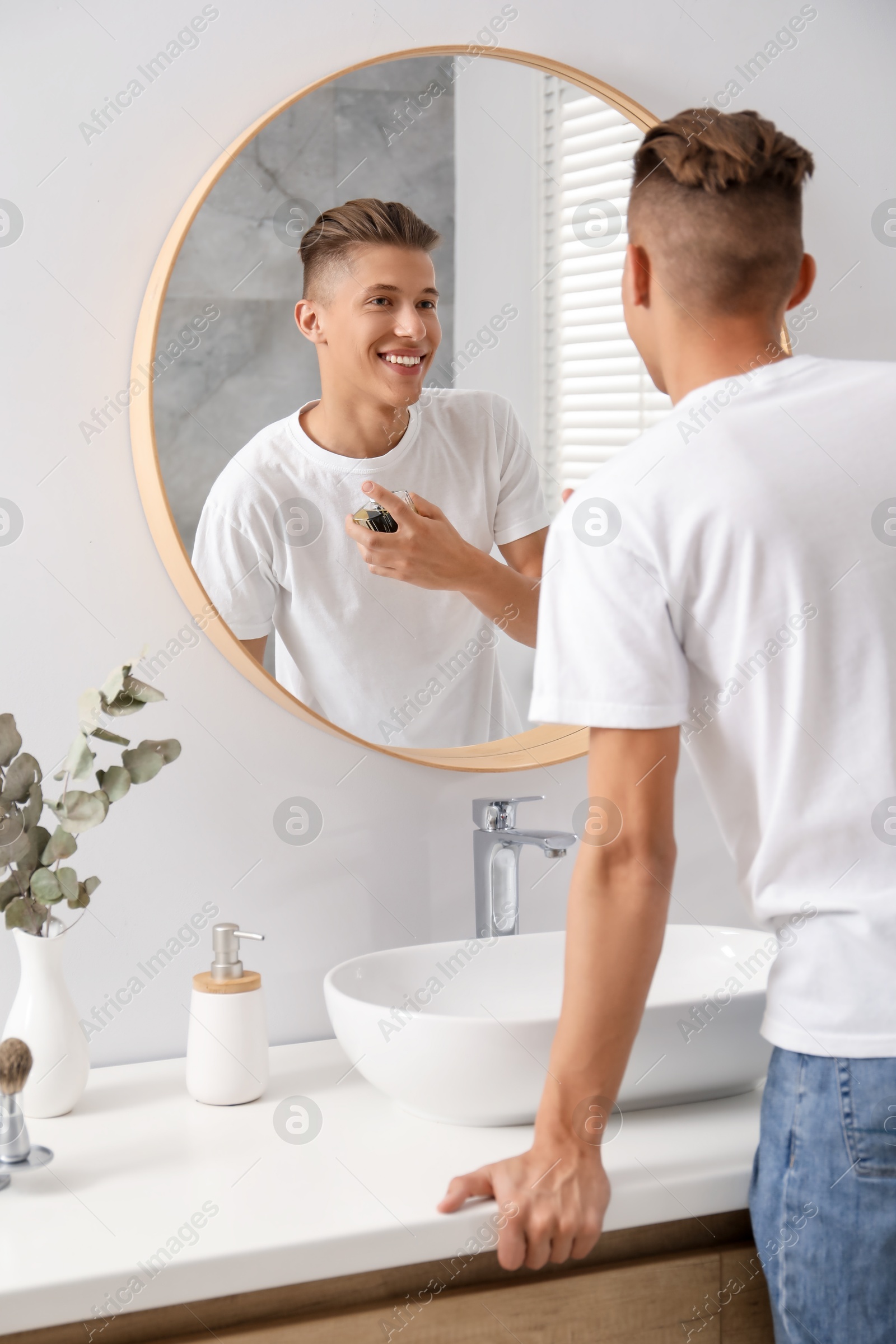 Photo of Man spraying luxury perfume near mirror in bathroom