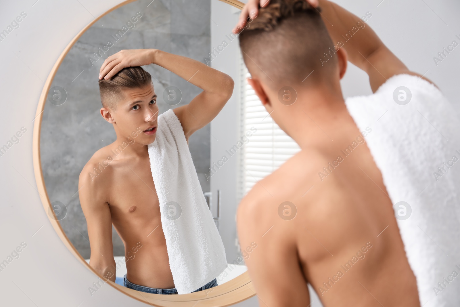 Photo of Handsome man with towel looking at mirror in bathroom