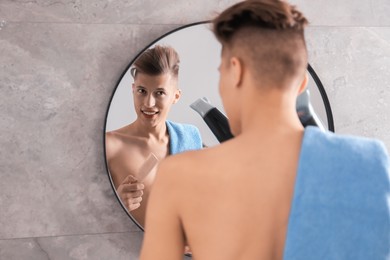 Photo of Handsome man using hair dryer near mirror in bathroom