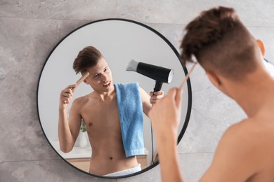 Photo of Handsome man using hair dryer near mirror in bathroom