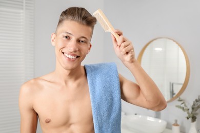 Handsome man with comb and towel in bathroom