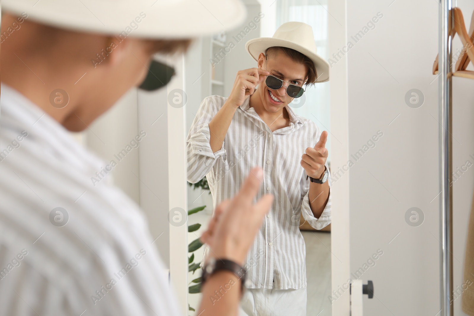 Photo of Handsome man in hat and glasses looking at mirror indoors