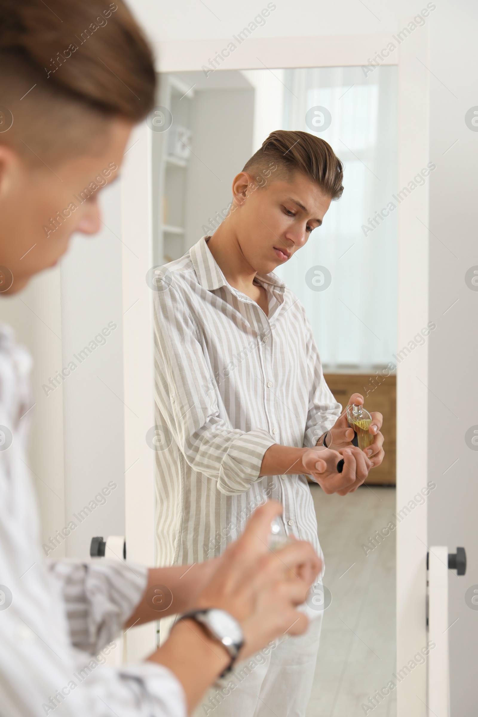 Photo of Man spraying luxury perfume near mirror indoors