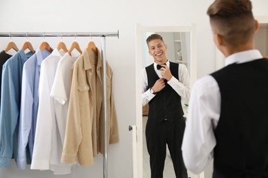 Photo of Handsome man adjusting bow tie near mirror indoors