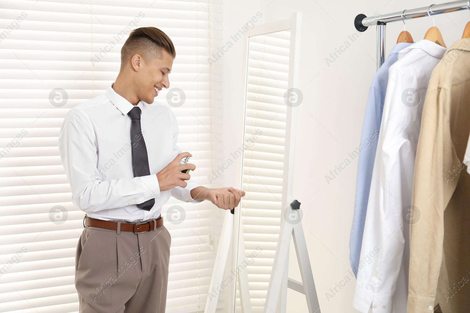 Photo of Man spraying luxury perfume near mirror indoors