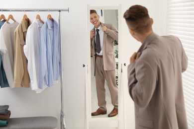 Photo of Handsome man in stylish suit looking at mirror indoors