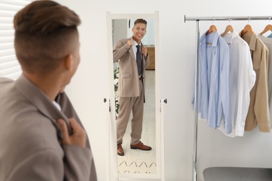 Handsome man in stylish suit looking at mirror indoors