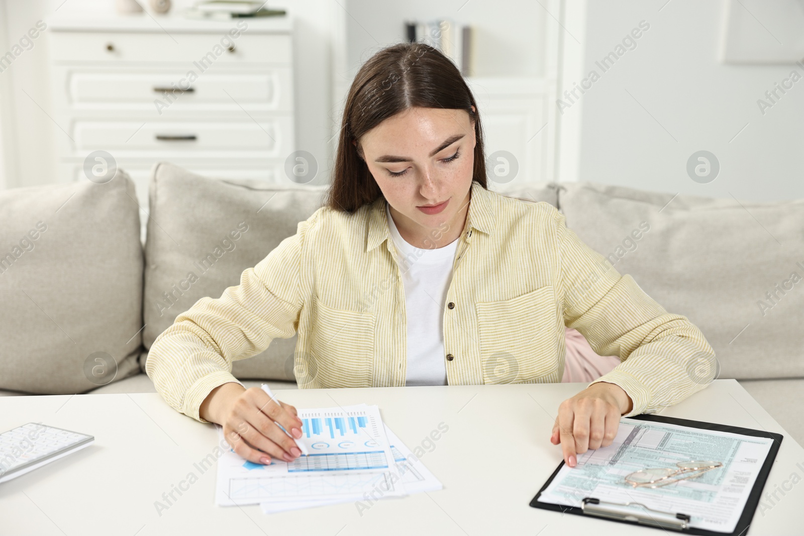 Photo of Budget planning. Beautiful young woman with papers at white table indoors