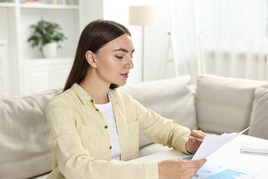 Budget planning. Beautiful young woman with papers at white table indoors