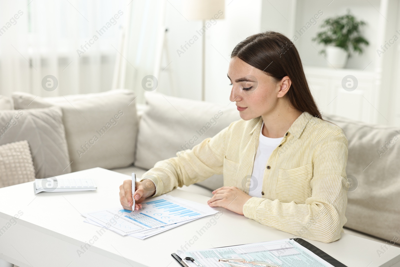 Photo of Budget planning. Beautiful young woman with papers at white table indoors