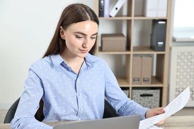 Photo of Budget planning. Beautiful young woman with papers and laptop at wooden table in office