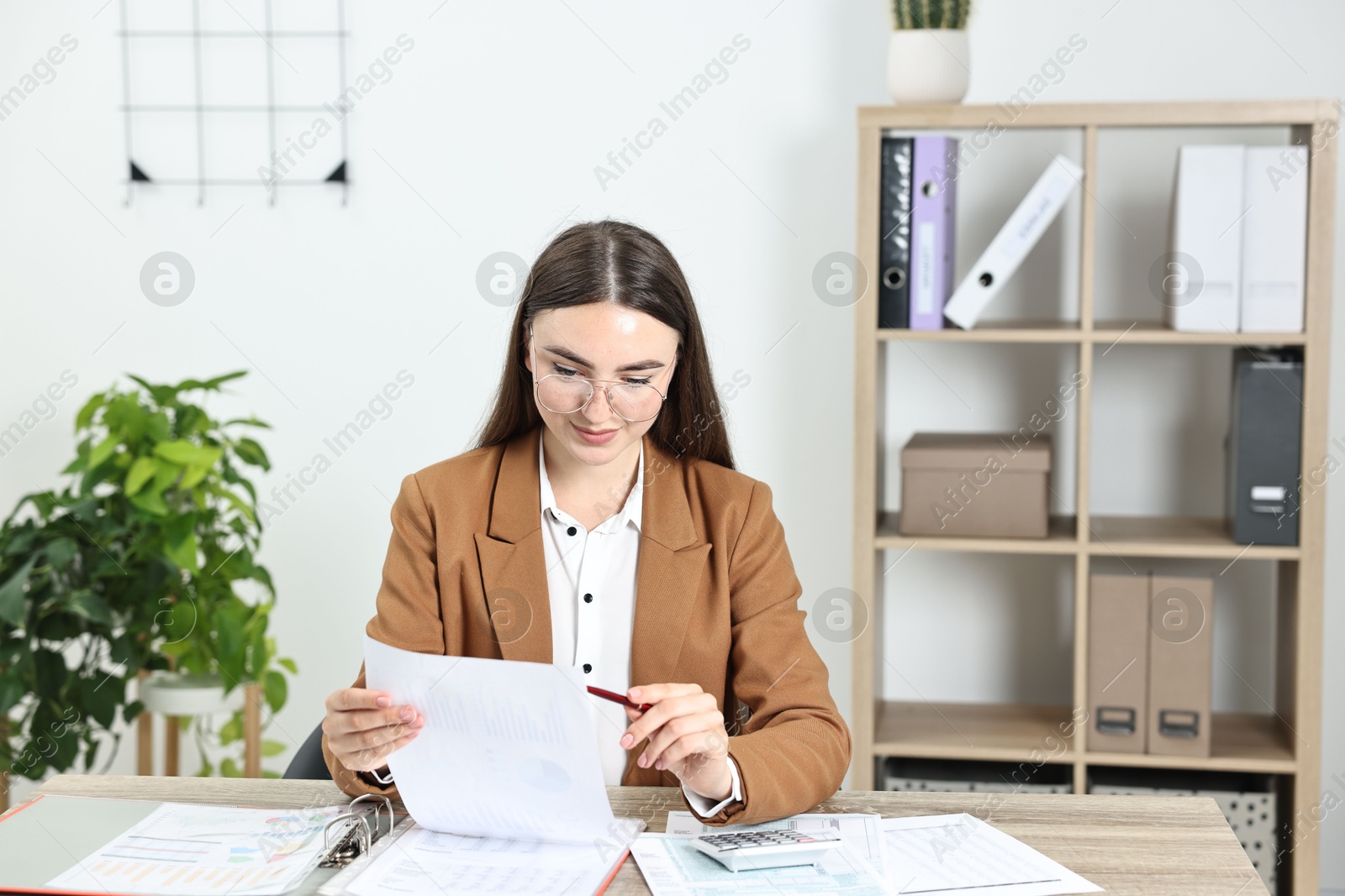 Photo of Budget planning. Beautiful young woman with papers and calculator at wooden table in office