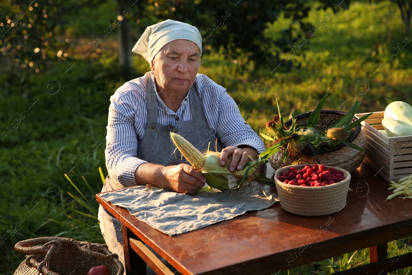 Photo of Senior farmer with different fresh products at wooden table outdoors