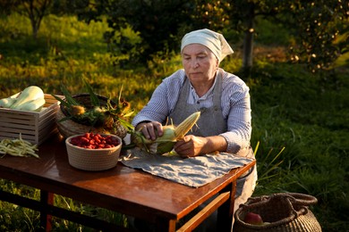 Photo of Senior farmer with different fresh products at wooden table outdoors