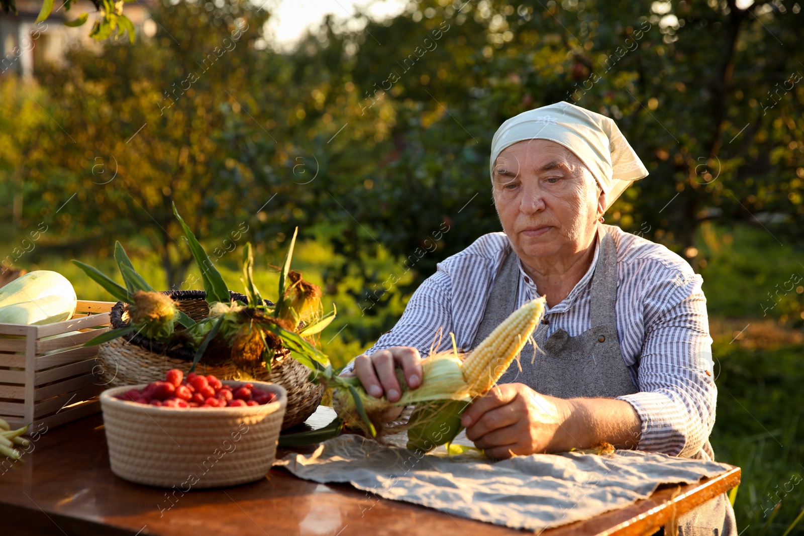 Photo of Senior farmer with different fresh products at wooden table outdoors