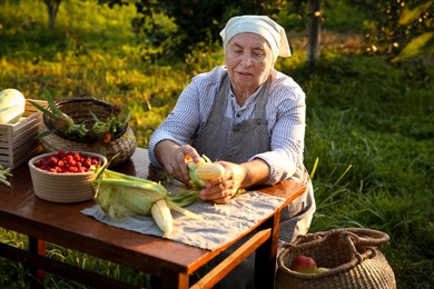 Photo of Senior farmer with different fresh products at wooden table outdoors