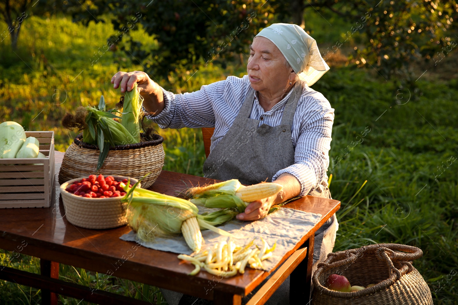 Photo of Senior farmer with different fresh products at wooden table outdoors