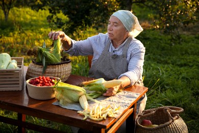 Senior farmer with different fresh products at wooden table outdoors