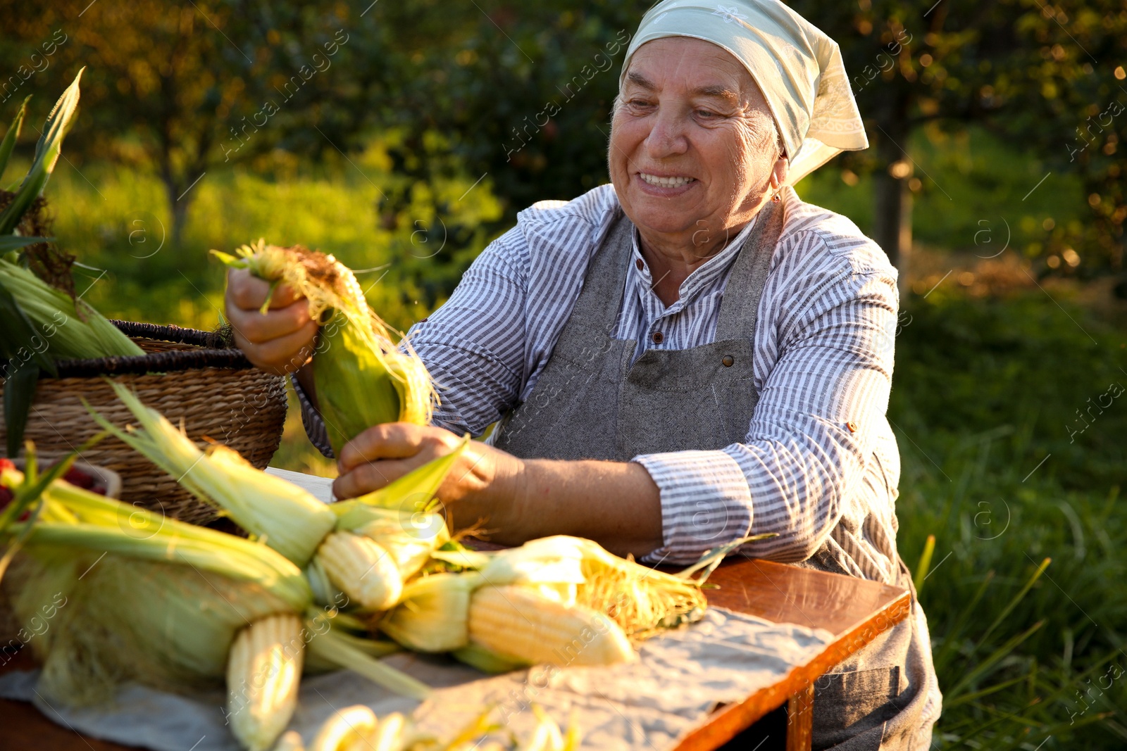 Photo of Senior farmer with different fresh products at wooden table outdoors