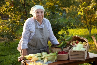 Photo of Senior farmer with different fresh products at wooden table outdoors