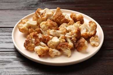 Photo of Plate with tasty baked cauliflower on wooden table, closeup