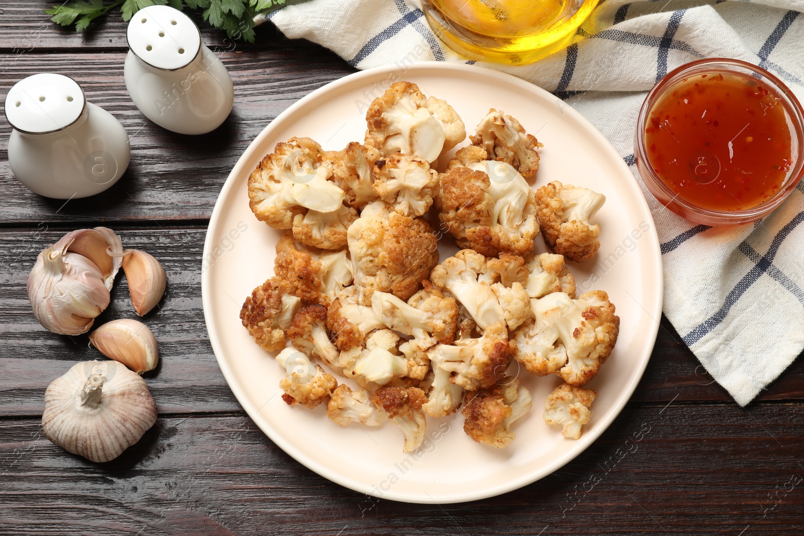 Photo of Plate with tasty baked cauliflower, garlic, sauce and spices on wooden table, flat lay