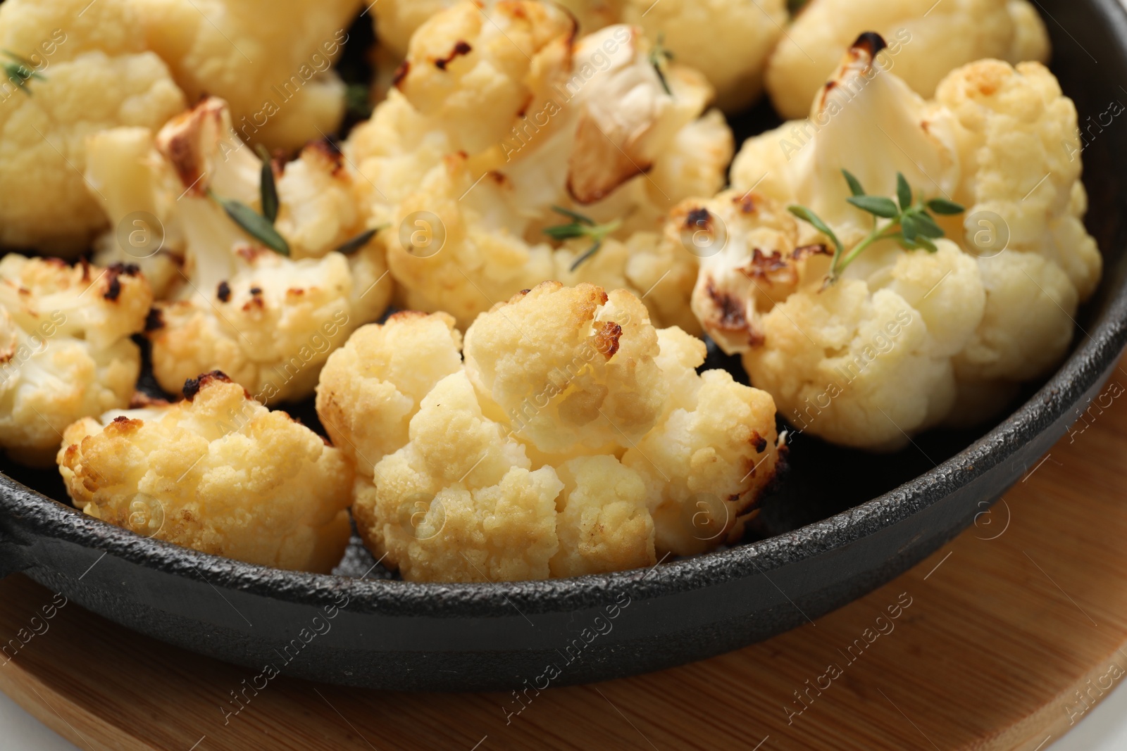 Photo of Tasty baked cauliflower with thyme in baking pan on wooden board, closeup