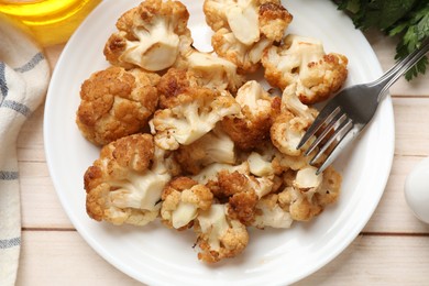 Photo of Plate with tasty baked cauliflower served on light wooden table, flat lay