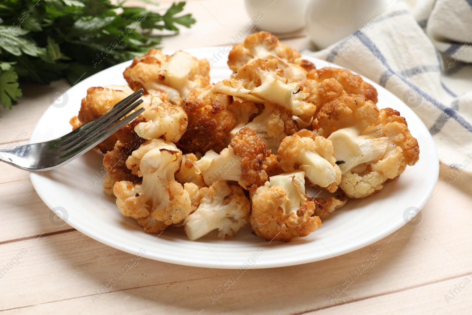 Photo of Plate with tasty baked cauliflower on light wooden table, closeup