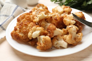 Plate with tasty baked cauliflower on light wooden table, closeup