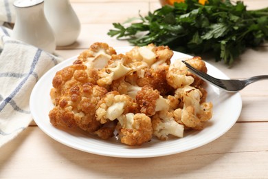 Photo of Plate with tasty baked cauliflower on light wooden table, closeup